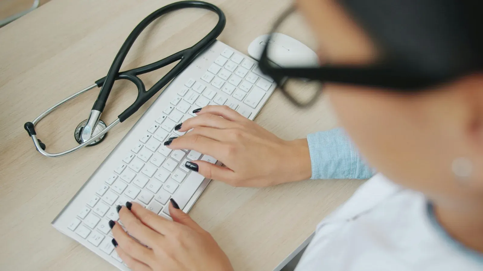 Doctor typing on keyboard with stethoscope nearby
